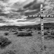 <i class="fa-regular fa-image orange1"></i> A estrada cruza o Deserto de Mojave, a oeste do Death Valley National Park (Califórnia, EUA). Perdida no meio do nada, essa cruz nos lembra a fragilidade do homem frente à natureza. / <em>The road cuts through the Mojave Desert, west of Death Valley National Park (California, USA). Lost in the middle of nowhere, this cross reminds us the fragility of man in the face of nature.</em> Edu Moreira - Ansel Adams