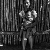 <i class="fa-regular fa-image orange1"></i> Celina (42 anos), sua casa e seu neto, aldeia Morro Falhado, São João das Missões, MG. / <em>Celina (42 years old), her house and grand son, Morro Falhado indigenous village, Sao Joao das Missoes, Minas Gerais.</em> Edu Moreira - Xacriabás