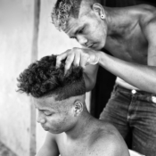 <i class="fa-regular fa-image orange1"></i> Giuso cortando o cabelo de um amigo, aldeia Riachinho, São João Missões, MG. / <em>Giuso having his friend's hair cut, Riachinho indigenous village, Sao Joao das Missoes, Minas Gerais.</em> Edu Moreira - Xacriabás